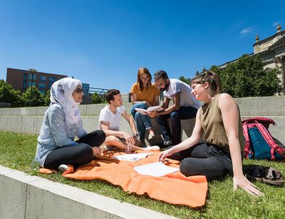 Students are seen relaxing outside on a blanket.