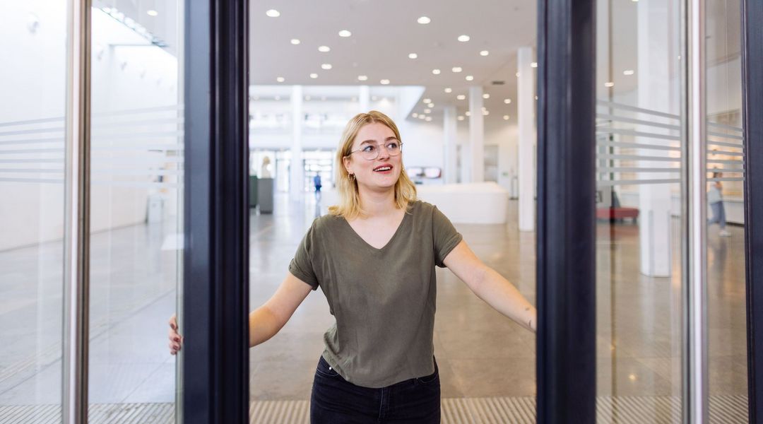 Studentin öffnet mit einem Lächeln die Tür zum Neuen Augusteum, Foto: Christian Hüller