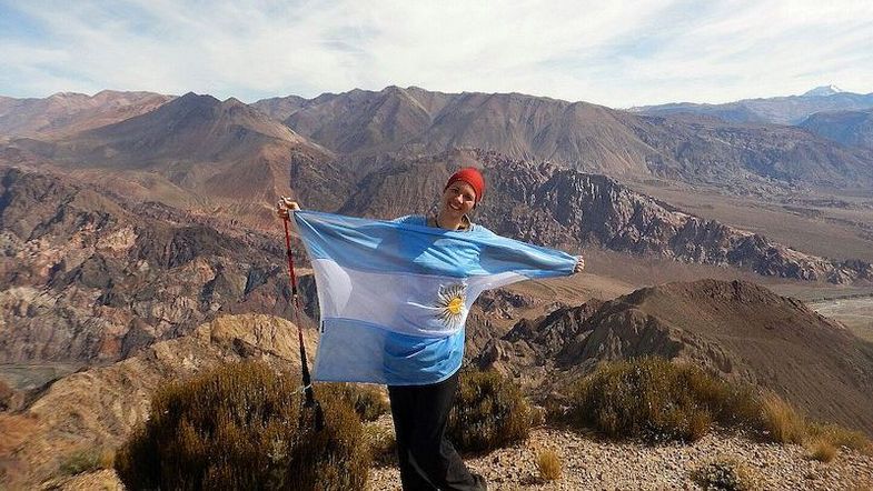 Farbfoto: Eine Person steht auf einem Berg und ist in die Argentinische Flagge gewickelt.