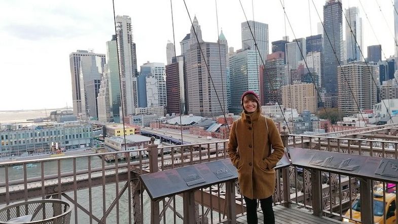 Farbfoto: Eine Person steht auf einer Aussichtsplattform in einer großen Stadt um sie herum stehen viele hohe Häuser, vor allem Wolkenkratzer.