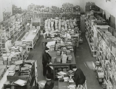 Schwarz-weiß-Foto: Ein Raum mit vielen Regalen voller Bücher und gestapelten Büchern