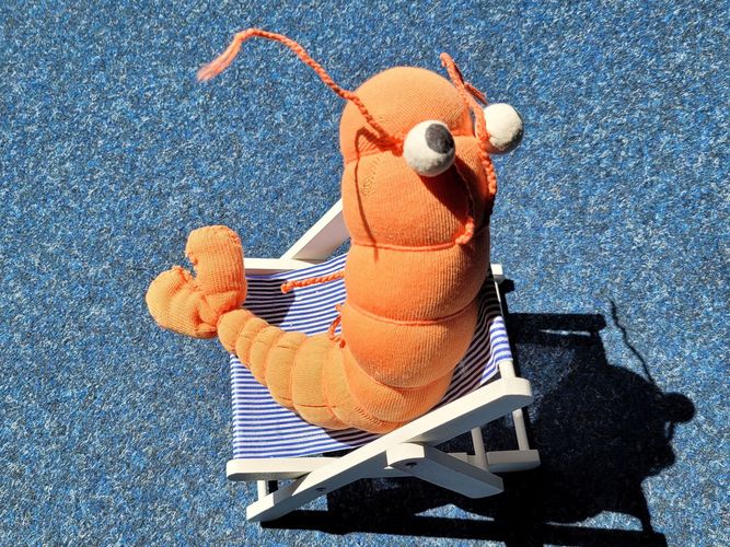 Orangefarbenes Stofftier in Form eines Shrimps in einem kleinen Liegestuhl