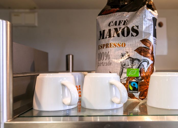 Zu sehen ist eine große Kaffeepackung mit dem Fairtrade-Siegel, daneben stehen leere Kaffeetassen.
