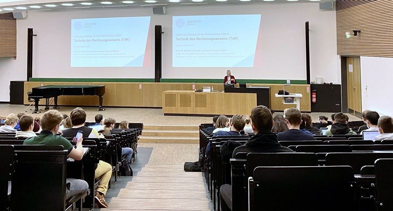 Einblick in den Hörsaal 9 mit Reihen voller Studierender und Lehrender vorn auf der Bühne