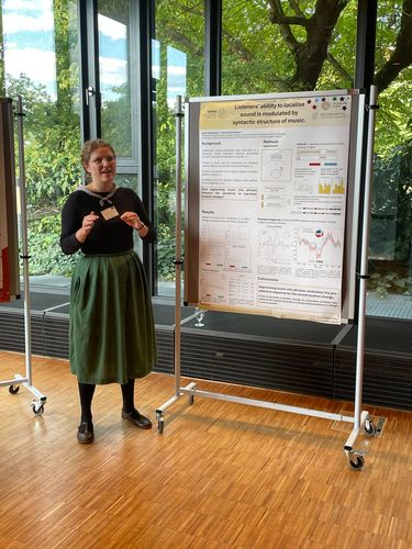 A woman standing in front of the scientific poster with the glass wall in the background.