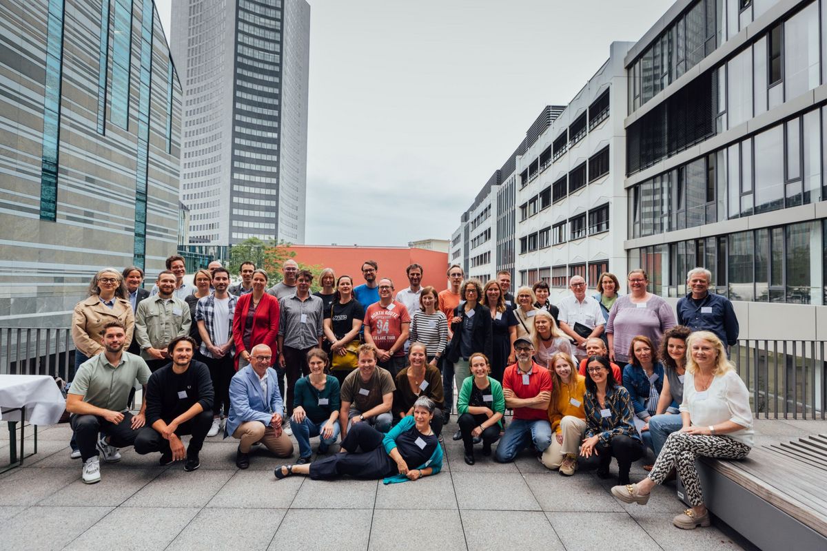 enlarge the image: Picture taken in daylight, outside, a large group of people standing together facing the camera, Leipzig University campus in the background