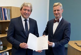 Wissenschaftsstaatssekretär Dr. Andreas Handschuh überreicht Dr. Jörg Wadzack eine Urkunde in einem Büro