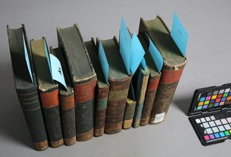 Zu sehen sind Bücherrücken, die grau gefärbt sind. Blaue Zettel markieren sie als Bücher unter Arsenverdacht.