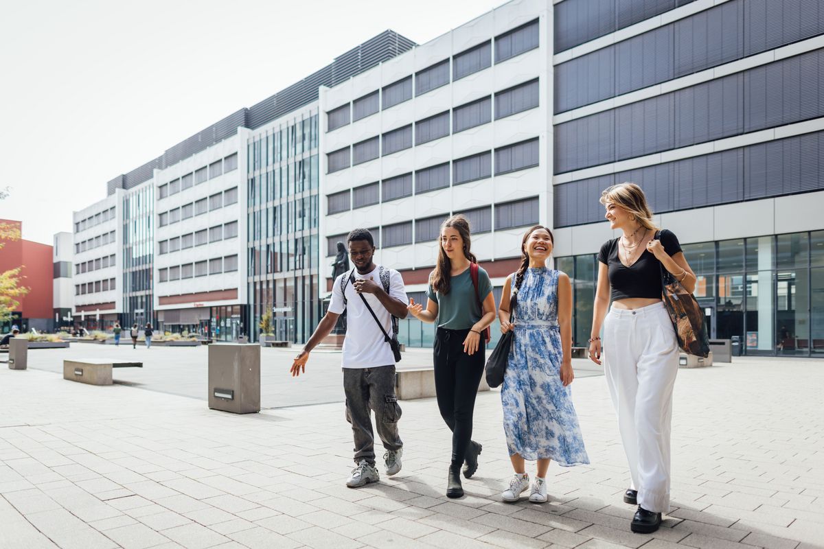 enlarge the image: Colour photo: Four people walking across the inner courtyard of the university and talking