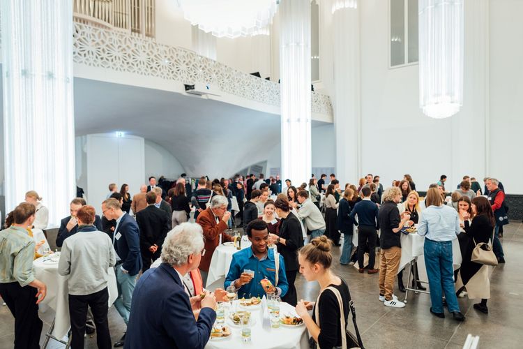 Förderer und Stipendiaten stehen an Stehtischen mit Essen und Getränken und unterhalten sich