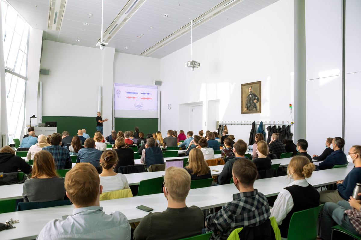 enlarge the image: A professor explaining a presentation slide in front of the symposium participants in a lecture hall