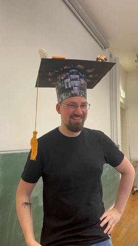 A man with a PhD hat standing and smiling