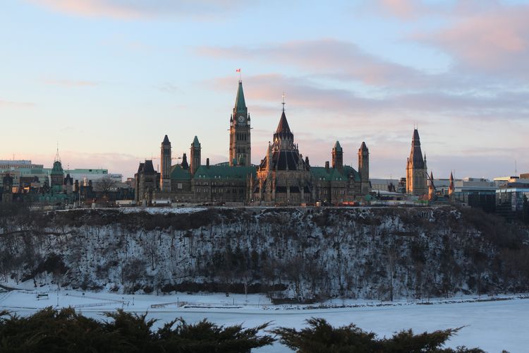 Ein imposantes Gebäude ragt auf einer Anhöhe empor. Es hat Ähnlichkeiten mit einer Burg, aber es handelt sich um das kanadische Parlament. Es ist aus hellbraunem Stein und die Spitzen Dächer sind blau, da das Kupfer der Spitzen oxidiert ist.