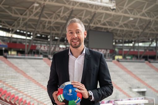 ZU sehen ist Stefan Schedler, der mit einem Fußball in der Hand im EM-Stadion steht.
