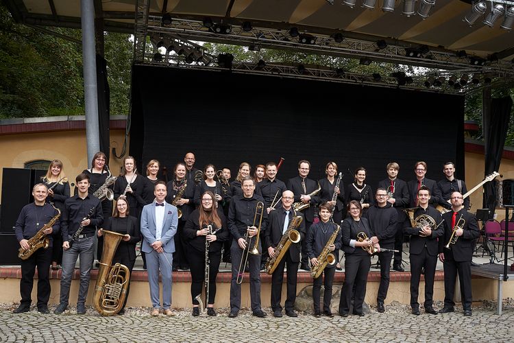 Frontalaufnahme Gruppenfoto des Blaswerk-Ensembles mit ihren Instrumenten vor der Bühne des Geyserhauses in Leipzig