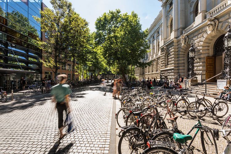 Studierende vor der Universitätsbibliothek. Ihre Umrisse sind unscharf, da sie in Bewegung sind