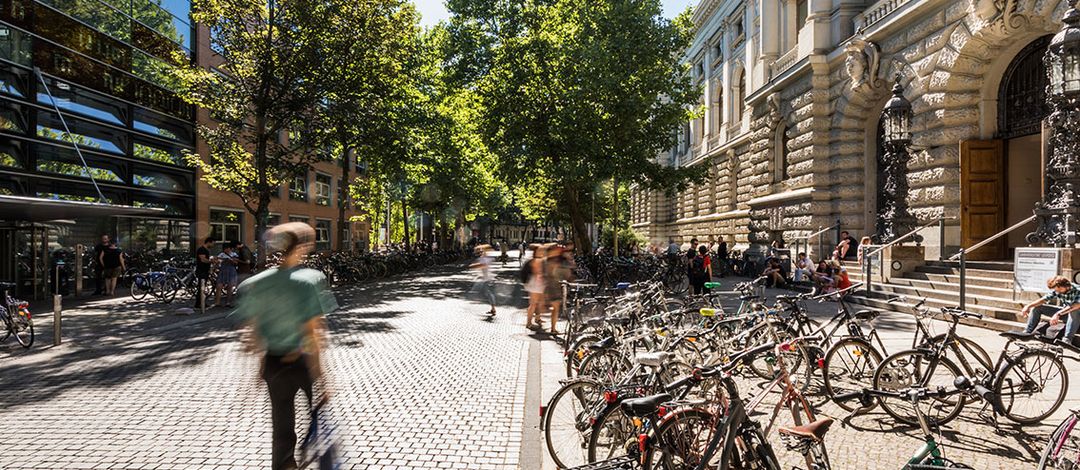 Studierende vor der Universitätsbibliothek. Ihre Umrisse sind unscharf, da sie in Bewegung sind